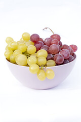White and red grapes in pink plastic bowl, white background.