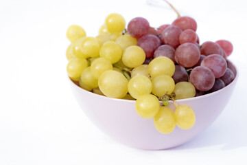 White and red grapes in pink plastic bowl, white background.