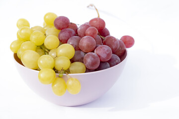 White and red grapes in pink plastic bowl, white background.