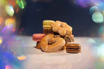 Vibrant macarons, cookies, and gingerbread rest on a white surface against a black backdrop,...