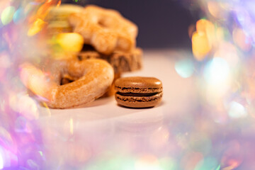 Vibrant macarons, cookies, and gingerbread on a white surface against a black backdrop, accented by twinkling lights, create a captivating bokeh effect. Ideal for bakery banners.