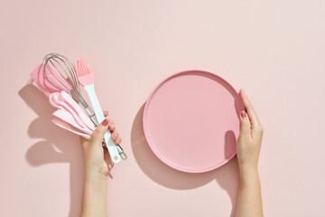 Woman hand holding kitchen utensils on pink background. Baking tools