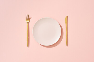 Knife, pastel pink plate and fork on pink background