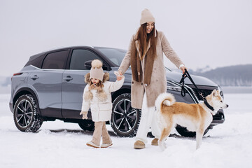 Woman with her daughter and dog having a walk in a snowy park by their car