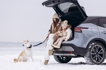Mother with her daughter and their dog sitting in trunk of car in a wintery weather