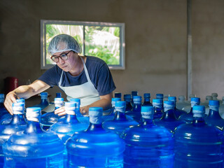 Asian man worker or quality inspector in workwear working in checking drinking water Blue gallon in drink water factory before shipment.drinking water business,small business,store,warehouse
