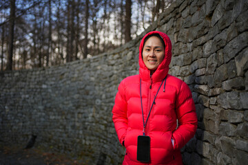 portrait of a smiling asian woman with a smartphone standing outdoors
