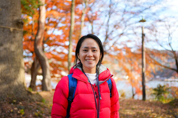 portrait of a smiling asian woman with a smartphone standing outdoors