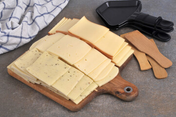 Tranches de fromage à raclette sur une planche à découper avec des ustensiles de cuisine