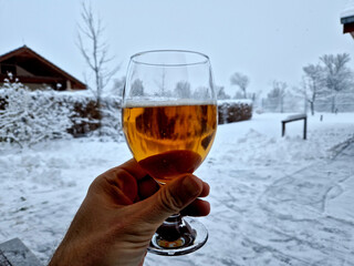 man takes a glass of beer and toasts his health in the middle of winter covered with snow. glass on a leg. a yellow gold color with a rich taste outdoors in nature