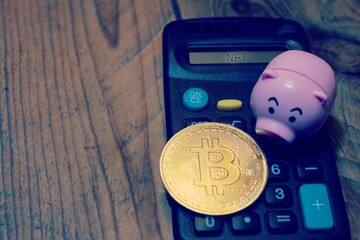 Calculator showing the text “Nft” with on top a piggy bank and a bitcoin. Concept of investing the savings on cryptocurrency .