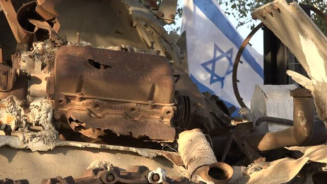 Closeup of the remains of a destroyed army tank, with a waving Israeli flag in the background (on the Golan Heights, 1967 Six Day War monument)
