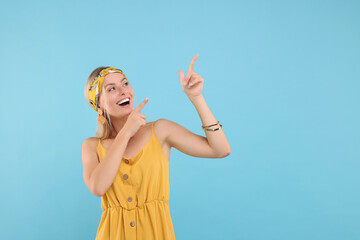 Portrait of happy hippie woman pointing at something on light blue background. Space for text