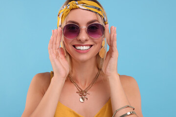 Portrait of smiling hippie woman in sunglasses on light blue background