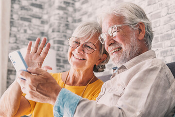 Happy retired family couple using mobile phone for video call together, talking to relations,...