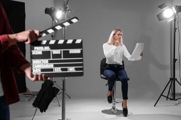 Casting call. Emotional woman performing while second assistance camera holding clapperboard against grey background in studio - obrazy, fototapety, plakaty