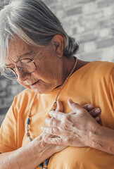 Obraz premium Upset stressed mature middle aged woman feeling pain ache touching chest having heart attack, sad worried senior older lady suffers from heartache at home, infarction or female heart disease concept.