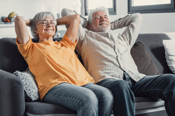 Peaceful middle aged man and woman with closed eyes relaxing on comfortable couch at home, mature family daydreaming together, grey haired wife and husband resting with hands behind head, breathing.