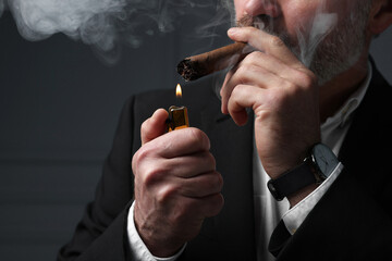 Bearded man lighting cigar on dark grey background, closeup - Powered by Adobe