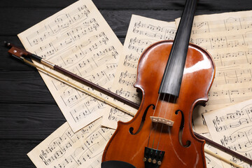Naklejka premium Violin, bow and music sheets on black wooden table, above view