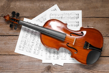 Violin and music sheets on wooden table, top view