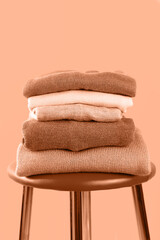 Warm knitwear in a pile on a chair on a peach background. Second hand, wardrobe sorting, cross-dressing, economic crisis, money saving, waste reduction, compassion, connection. - obrazy, fototapety, plakaty