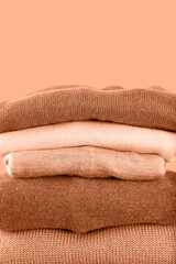 A pile of warm knitwear to keep you warm in winter on a peach background. Cross-dressing, economic crisis, saving money, reducing waste, fast fashion free, compassion, connection. - obrazy, fototapety, plakaty