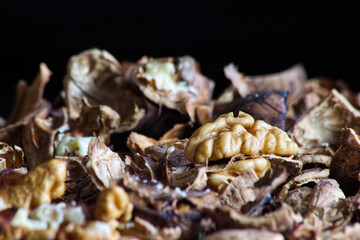 Walnut kernel mixed with broken shells spread over the table close-up on dark background.