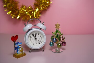 decorative interior decorations in the form of a dragon figurine near the clock and a glass Christmas tree on a pink background with a golden garland with a free place for the inscription