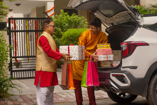 Grandfather and grandson unloading Diwali gifts from car trunk after shopping