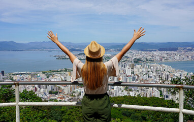 Tourism in Florianopolis, Brazil. Tourist woman with raising arms from belvedere in Florianopolis city, Santa Catarina, Brazil. - obrazy, fototapety, plakaty