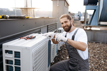 Close up of serious skilled repairman screwing bolt into air conditioner using screwdriver on roof...