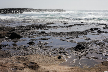 Rocky shore background. Volcanic rock on ocean shore. Tenerife on Canary island landscape. Sea wave crushing. Water white foam. Turbulent ocean background.
