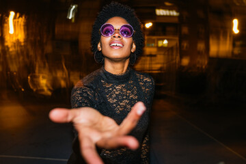 Happy black woman with afro and purple shades enjoys a night out, exuding positivity and style.