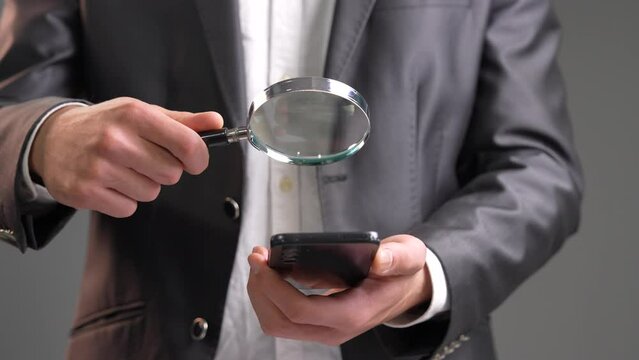 Dive into the intriguing world of technology and curiosity with this engaging stock video featuring a man examining his smartphone using a magnifying glass. The scene unfolds with a close-up of the in