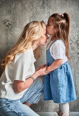 Side view of cute child kissing mother while standing against the wall at home. Blonde woman...