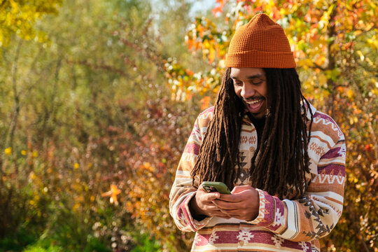 African American young man with dreadlocks happy using the smartphone in a sunny day of autumn.