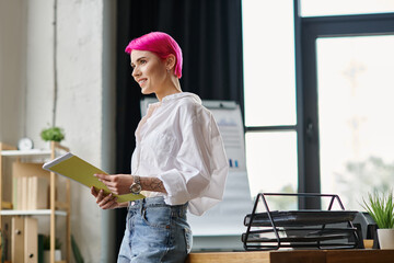 cheerful attractive female worker holding her notes at office and smiling happily, business concept