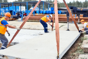 Professional builders work on construction site. Team of slingers lay concrete slab on ground on...