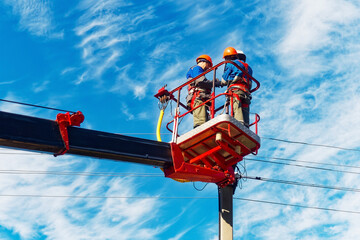 Two electricians from cradle of aerial platform or crane are repairing street lighting lamp....