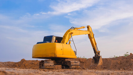 Obraz premium Yellow excavator is leveling the ground for construction area of industrial building in construction site against blue sky background