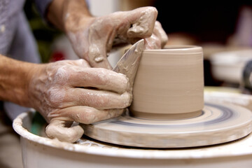 male hands making ceramic cup on pottery wheel with special wooden tool, Close-up