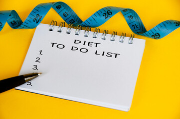 Diet to do list text on white notepad with blue measuring tape on yellow background. Health and diet concept
