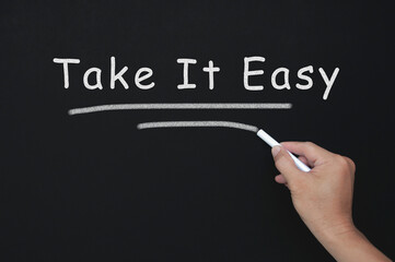 Take it easy text on blackboard with hand holding chalk.