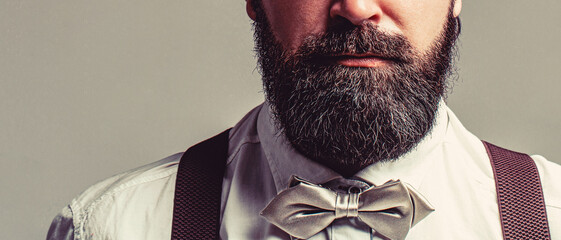 Close-up of a gentleman his bowtie. Beard man in bow tie and suspenders. Male in shirt correcting...