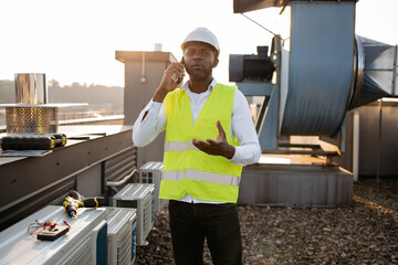 African american serious engineer wearing white helmet standing and having conversation on modern...
