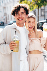 Young smiling beautiful woman and her handsome boyfriend in casual summer clothes. Happy cheerful family. Female having fun. Couple posing in street. Holding and drinking cocktail drink in plastic cup