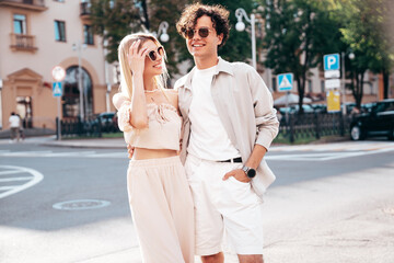 Fototapeta premium Young smiling beautiful woman and her handsome boyfriend in casual summer clothes. Happy cheerful family. Female having fun. Couple posing in the street background at sunny day. In sunglasses
