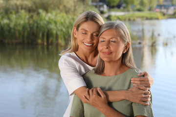Fototapeta na wymiar Family portrait of happy mother and daughter hugging near pond. Space for text