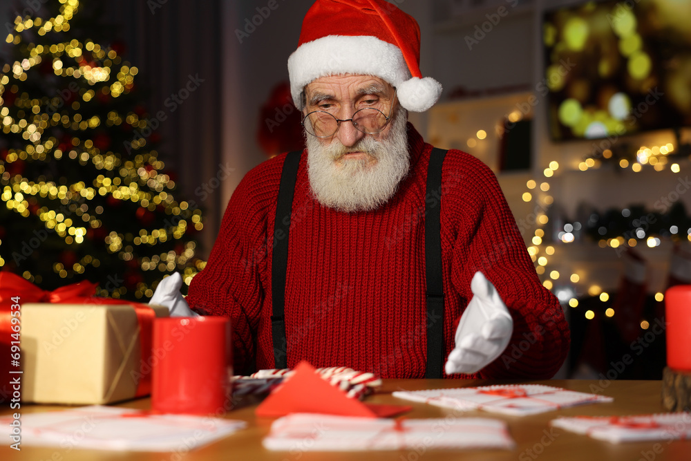 Wall mural Santa Claus at his workplace. Letters and gift box on table in room with Christmas tree